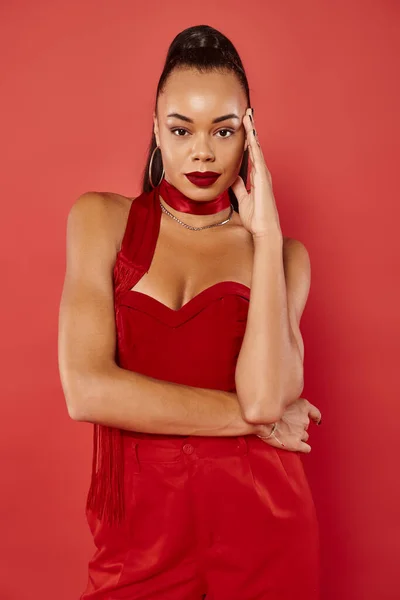 Beautiful african american woman in vibrant strapless top and pants posing on red background — Stock Photo
