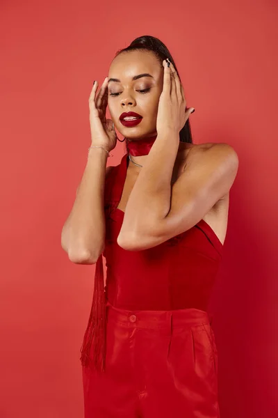 Hermosa modelo afroamericano en la parte superior sin tirantes vibrante y pantalones posando sobre fondo rojo - foto de stock