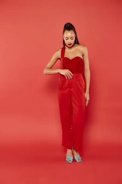 Pleine longueur de beau modèle afro-américain en haut sans bretelles et pantalon posant sur fond rouge — Photo de stock