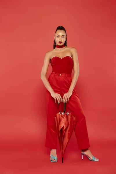 Comprimento total de encantador modelo americano africano em top strapless vermelho e calças posando com guarda-chuva — Fotografia de Stock