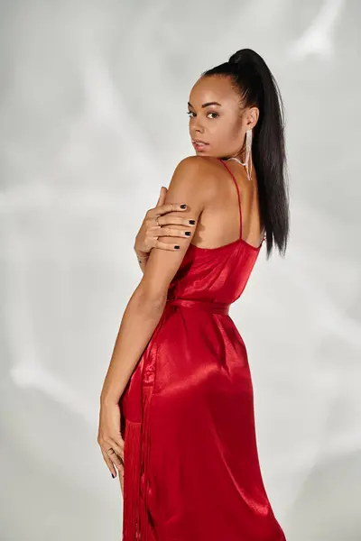 Alluring african american woman in red dress looking at camera and posing on mirrored grey backdrop — Stock Photo