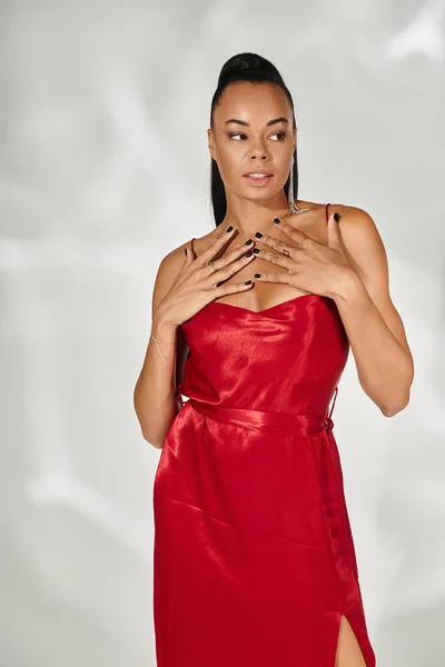 Élégante femme afro-américaine en robe rouge regardant la caméra et posant sur fond gris miroir — Photo de stock
