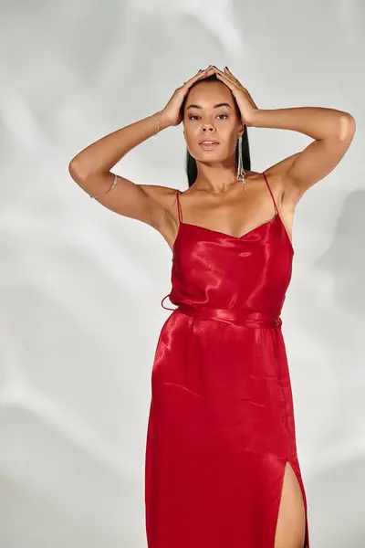 Femme afro-américaine confiante en robe rouge regardant la caméra et posant sur fond gris miroir — Photo de stock