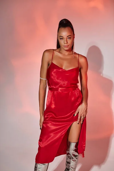 Femme afro-américaine sophistiquée en robe rouge regardant la caméra sur fond gris avec éclairage — Photo de stock