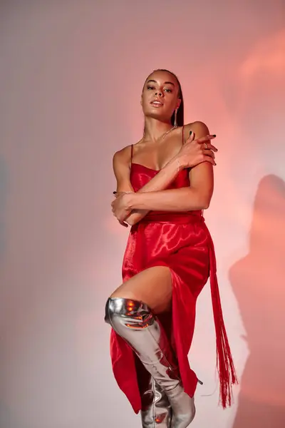 Stylish african american woman in midi red dress and silver boots on grey backdrop with lighting — Stock Photo