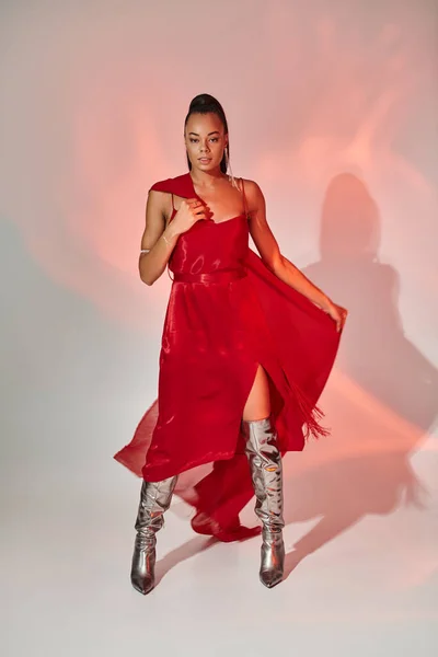 African american woman in red dress with shawl standing in silver boots on grey with lighting — Stock Photo