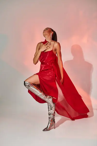Young african american woman in red dress with shawl posing in silver boots on grey with lighting — Stock Photo