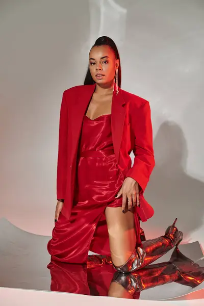 Young african american woman in red dress, blazer and silver boots posing on mirrored surface — Stock Photo