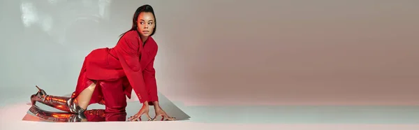 Afrikanisch-amerikanisches Model in rotem Blazer, Kleid und silbernen Stiefeln posiert auf verspiegelter Oberfläche, Banner — Stockfoto