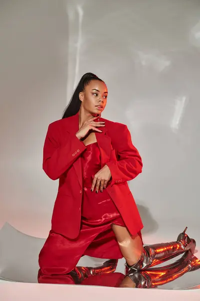 Young african american woman in red blazer, dress and silver boots posing on mirrored surface — Stock Photo