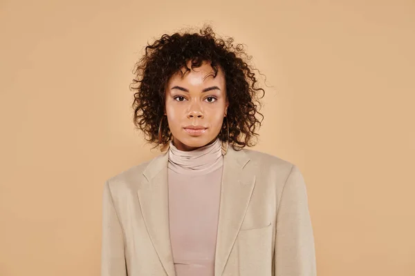 Beautiful african american woman with curly hair posing in autumnal blazer on beige backdrop, banner — Stock Photo