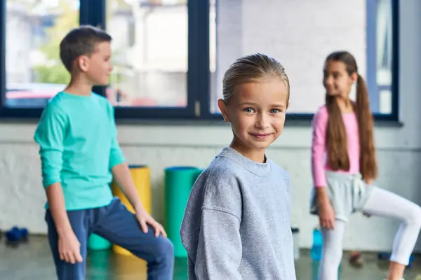 Pretty girl looking at camera with her two friends on backdrop while exercising, child sport — Stock Photo