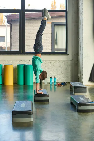 Vertikale Aufnahme eines kleinen Jungen in Sportbekleidung, der auf seinen Händen auf Fitness-Stepper im Fitnessstudio steht, Sport — Stockfoto