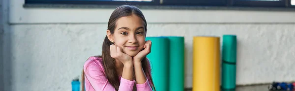 Счастливая маленькая девочка, сидящая и весело улыбающаяся на камеру, руки под подбородком, детский спорт, баннер — стоковое фото