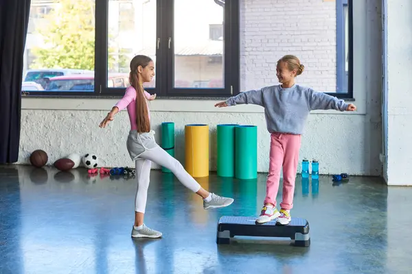 Zwei fröhliche kleine Mädchen in Sportbekleidung, die sich die Arme ausstrecken und einander anlächeln, Kindersport — Stockfoto