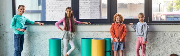 Niños y niñas lindos preadolescentes en ropa deportiva posando por la ventana en el gimnasio, deporte infantil, pancarta - foto de stock