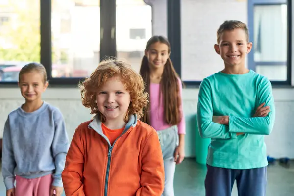 Cuatro niños preadolescentes alegres posando en el gimnasio y sonriendo alegremente a la cámara, deporte infantil - foto de stock