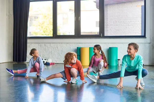 Four preadolescent cute boys and girls stretching their legs and smiling at each other, child sport — Stock Photo