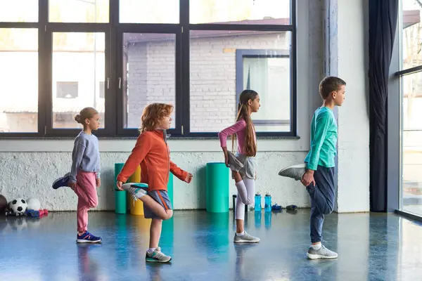 Чотири підлітка гарненькі діти в спортивному одязі, що розтягують ноги в спортзалі, дитячий спорт — стокове фото