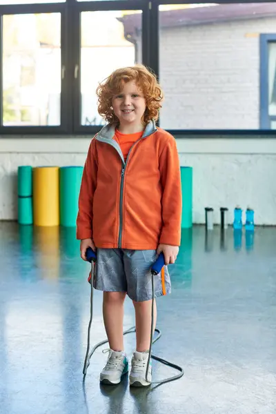 Alegre menino ruivo posando com pular corda e sorrindo alegremente para a câmera, esporte infantil — Fotografia de Stock