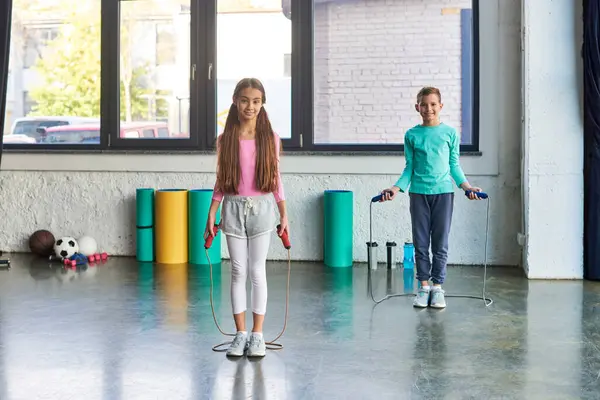 Kleine süße Jungen und Mädchen in Sportbekleidung posieren mit Springseilen und lächeln in die Kamera, Kindersport — Stockfoto