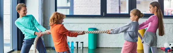 Quatro crianças bonitas em sportswear jogando rebocador de guerra com corda fitness no ginásio, esporte infantil, bandeira — Fotografia de Stock