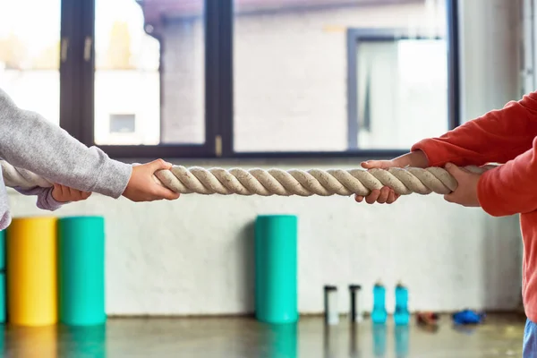 Vista recortada de dos niños preadolescentes en ropa deportiva tirando de la cuerda de fitness en el gimnasio, deporte infantil - foto de stock