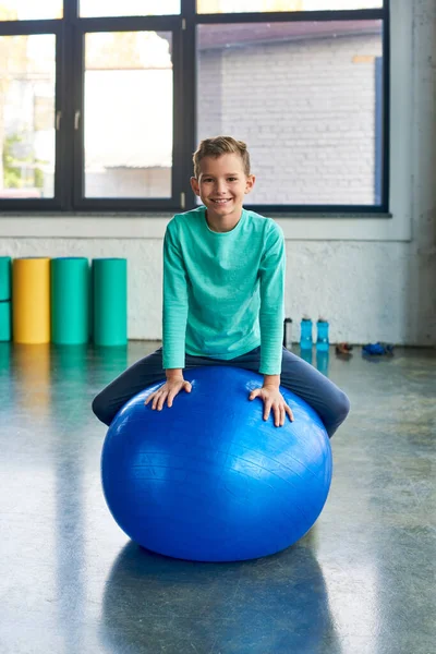 Bonito niño en entrenamiento de ropa deportiva en la pelota de fitness y sonriendo a la cámara, deporte infantil - foto de stock