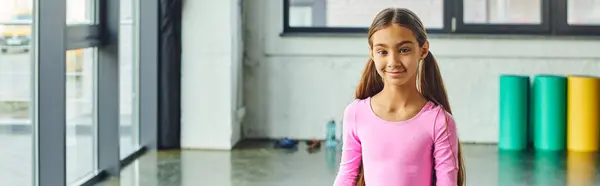 Alegre preadolescente linda chica con el pelo largo en ropa deportiva sonriendo a la cámara, deporte infantil, pancarta - foto de stock