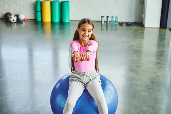 Preadolescente linda chica en rosa ropa deportiva ejercicio con mancuerna en la pelota de fitness, deporte infantil - foto de stock
