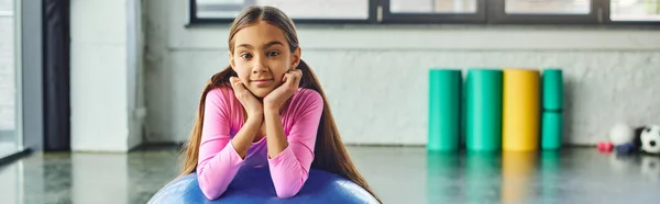 Lustiges kleines Mädchen mit langen Haaren posiert mit Fitnessball mit Händen unterm Kinn, Kindersport, Banner — Stockfoto