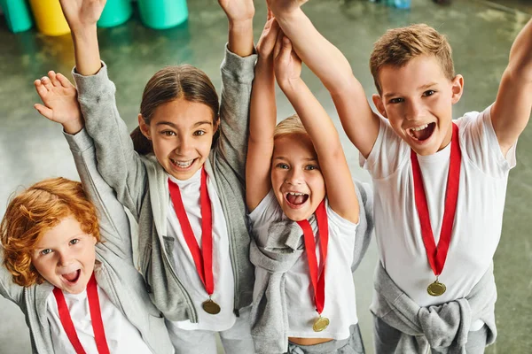 Niños y niñas felices en ropa deportiva con medallas de oro animando y sonriendo a la cámara - foto de stock
