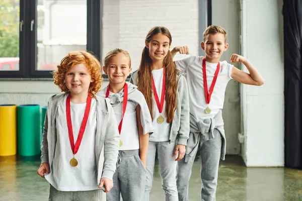 Joyous children in sportswear with golden medals smiling cheerfully at camera, child sport — Stock Photo
