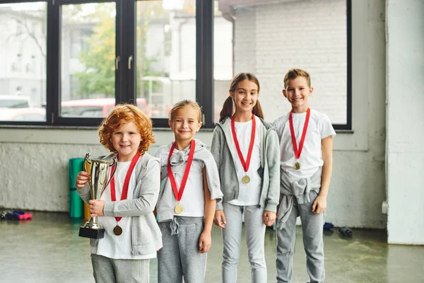 Niñas y niños alegres sonriendo y posando con trofeo y medalla de oro, deporte infantil - foto de stock