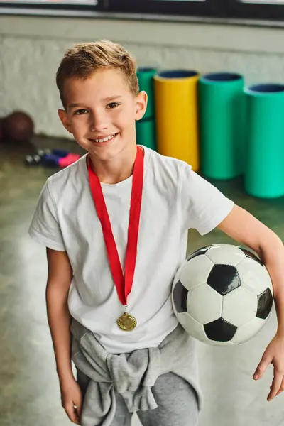 Tiro vertical de menino com medalha de ouro e bola de futebol com tapete de fitness no fundo, esporte — Fotografia de Stock