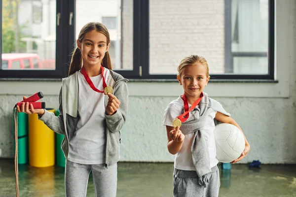 Cute preadolescent girls posing with golden medals with jump rope and volleyball in hands, sport — Stock Photo