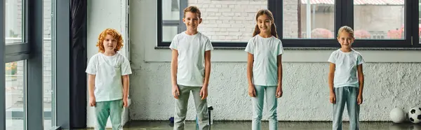 Jolly little children in sportswear posing in gym with window on backdrop, child sport, banner — Stock Photo