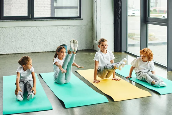 Süße vorpubertäre Kinder in Sportbekleidung, die ihre Muskeln dehnen und fröhlich lächeln, Sport — Stockfoto