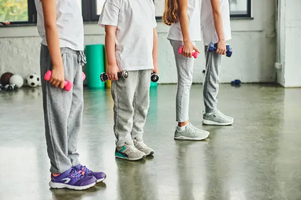 Vista ritagliata di bambini preadolescenti in abbigliamento sportivo esercizio con manubri, sport infantile — Foto stock