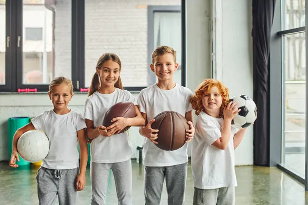 Allegri bambini piccoli che tengono diversi tipi di palle e sorridono alla macchina fotografica, sport per bambini — Foto stock