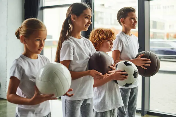 Четыре милые preadolescent детей с различными видами шариков позировать в профиль, детский спорт — стоковое фото