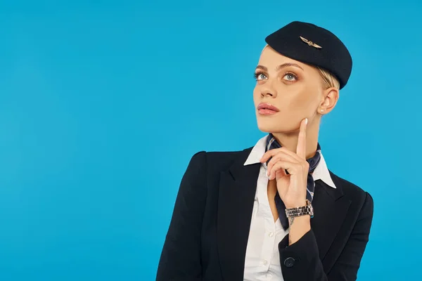 Вдумчивая стюардесса в стильной униформе, трогательная физиономия и взгляд в сторону, стоя на синем фоне — стоковое фото