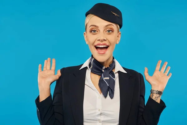 Ritratto di hostess stupita e gioiosa in uniforme mostrando gesto wow su sfondo blu — Foto stock