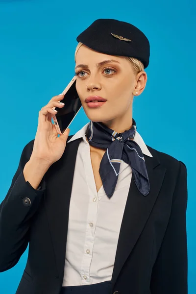 Hostess seria in uniforme elegante che parla al cellulare sul blu, lavora nel settore del trasporto aereo — Foto stock