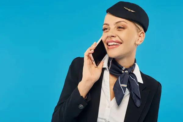 Hôtesse de l'air joyeuse en uniforme d'entreprise parler sur téléphone mobile sur fond bleu studio — Photo de stock