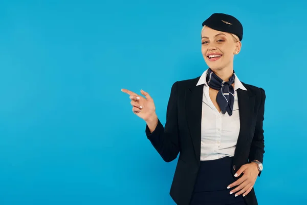 Lächelnde Stewardess zeigt weg, während sie die Richtung angibt und in die Kamera auf blauem Hintergrund schaut — Stockfoto
