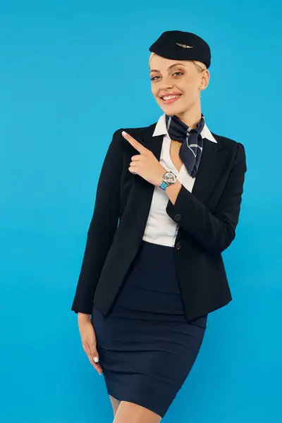 Fröhliche Stewardess zeigt weg und zeigt Richtung, während sie in die Kamera auf blauem Hintergrund schaut — Stockfoto