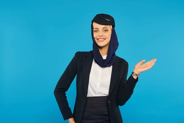 Arabian airlines hospitality, smiling stewardess in headscarf and uniform showing direction on blue — Stock Photo