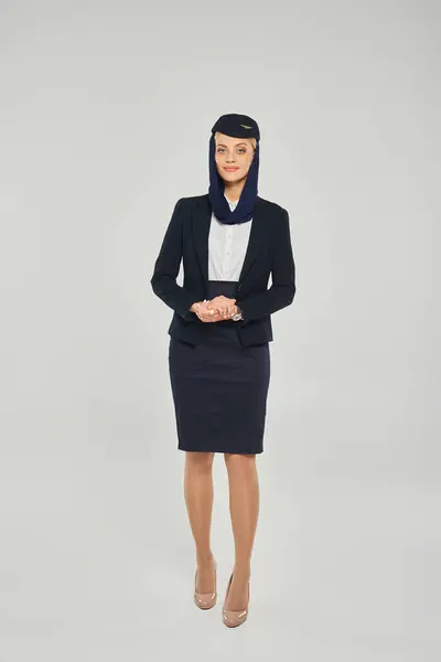Full length of young woman in elegant uniform of arabian airlines stewardess on grey backdrop — Stock Photo
