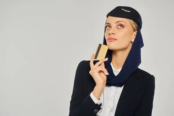 Thoughtful arabian airlines stewardess in uniform holding credit card and looking away on grey — Stock Photo